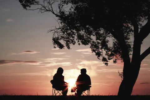 a couple sitting on a bench at sunset