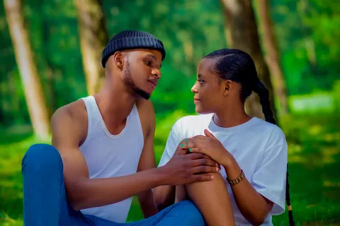 Young couple sitting on a picnic blanket with fruits, sharing a tender moment in a green forest park.