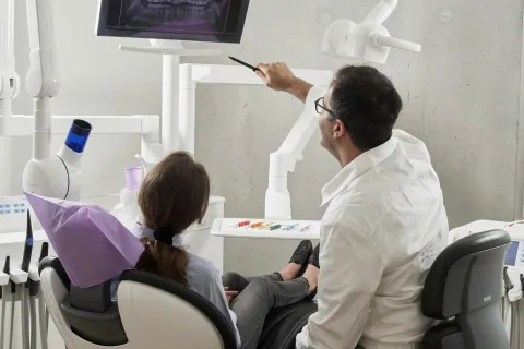 Dentist showing patient dental X-ray images on screen during consultation in modern dental clinic