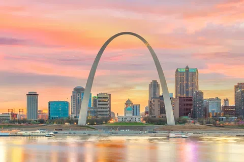 St. Louis Gateway Arch with city skyline and colorful sunset reflected on the Mississippi River.