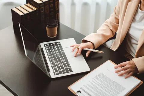 Person working on a laptop reviewing documents with a pen and coffee on a black desk
