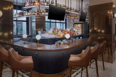 The Lowline by Hyatt JDV Hotel Custom Bar Millwork, Suspended Metal-and-Glass Liquor Shelving, Decorative Metal Focal Walls, and Island Quartz Countertop