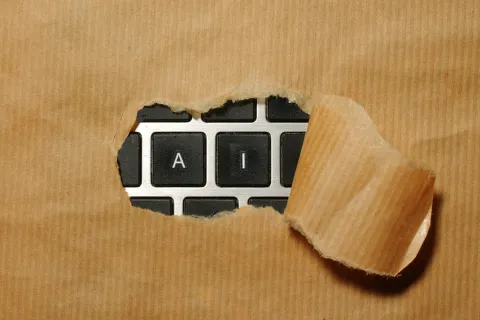 Close-up of keyboard keys 'A' and 'I' revealed through torn brown paper highlighting artificial intelligence concept.