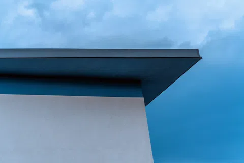 Minimalist building corner with flat overhang against a cloudy sky and blue background.