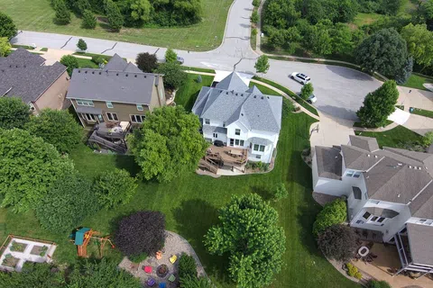 Aerial view of suburban neighborhood with houses, green lawns, trees, playground and curved roads on a sunny day