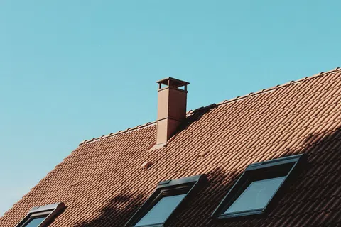 Brown tiled roof with skylights and chimney under clear blue sky in daylight.