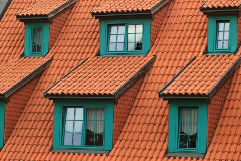 Close-up of orange tiled rooftops with green-framed windows on a series of houses under daylight.