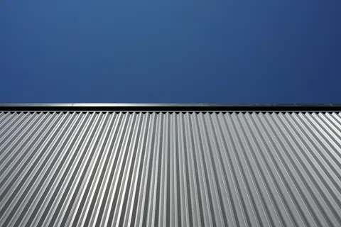 Silver metal building facade with vertical ridges under clear blue sky on a sunny day