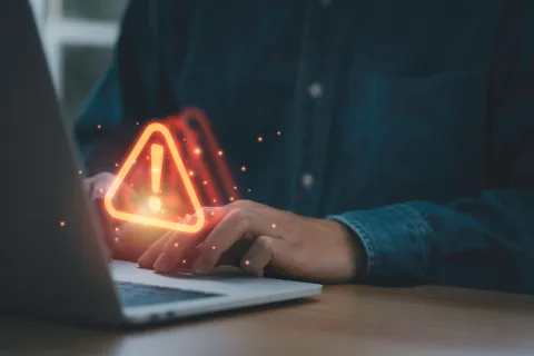 Person typing on laptop with glowing warning alert icon indicating an error or security issue.