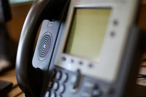 Close-up of a modern business phone handset and blurred digital display with keypad in the background.