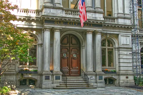 A local Historic Old City Hall building facade with large wooden doors, stone columns, American flag.