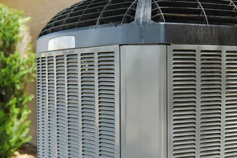 Close-up of a residential outdoor air conditioning unit with metal vents and a protective grille on top.