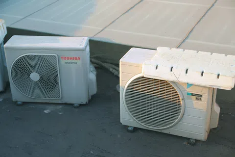 Two outdoor air conditioning units placed on a flat rooftop under sunlight with visible vents and branding.