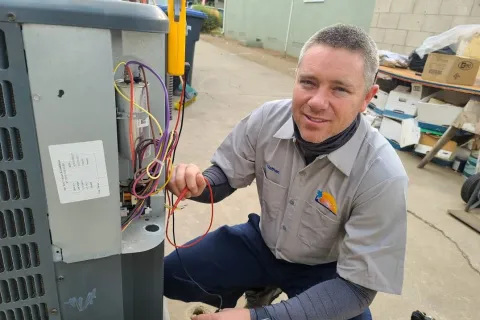 Technician wearing a sun hat and mask services a York HVAC unit on a rooftop with tools and hoses connected.