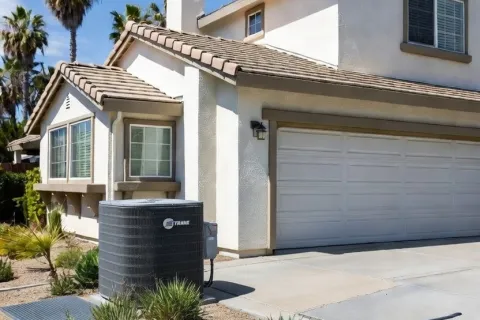 Two-story beige house with tiled roof, desert landscaping, and a central air conditioning unit on a sunny day.