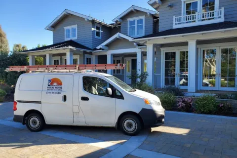 White Total Home Environmental service van parked in front of a modern two-story gray house with large windows.