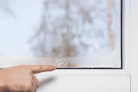 Hand pointing at condensation on a window pane from humidity