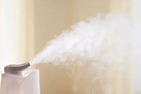 White humidifier releasing mist into a softly lit room with a beige background