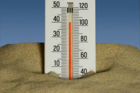 Thermometer in sand showing temperature around 36 degrees Celsius on a clear sunny day.
