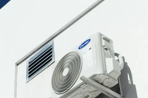 Outdoor Carrier air conditioning unit mounted on white building wall under clear blue sky.