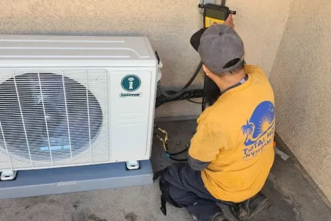 Technician installing or repairing an outdoor air conditioning unit on a concrete surface near a stucco wall.
