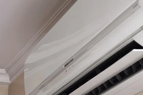 Modern white wall-mounted air conditioner unit installed near ceiling for indoor cooling.