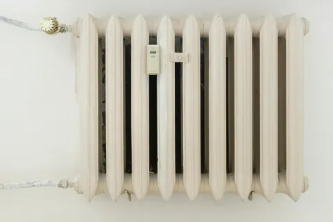 White vintage cast iron radiator heater mounted on a white wall with pipe connections and a control valve.