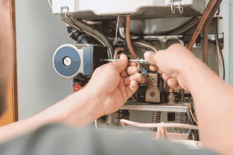 Technician repairing or maintaining a boiler with tools and visible internal components in a close-up view.