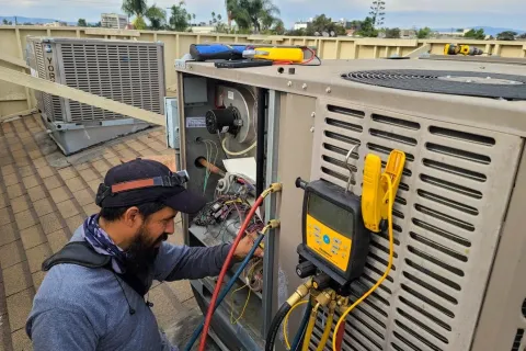 Technician inspecting and repairing rooftop HVAC unit with diagnostic tools and gauges during maintenance work.