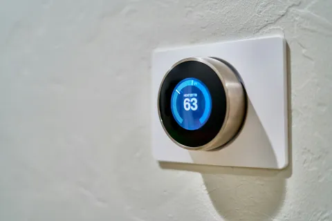Close-up of a smart thermostat displaying a heat setting of 63 degrees on a wall-mounted control panel.