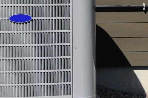 Gray outdoor air conditioning unit installed on concrete slab beside house with wooden siding.