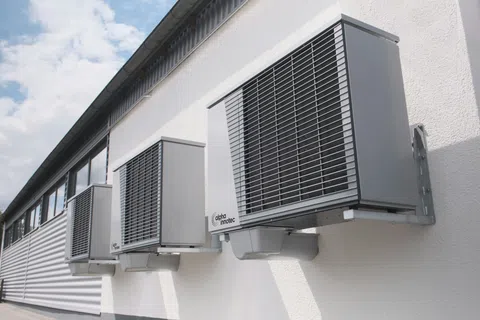 Three modern gray air conditioning units mounted on the exterior white wall of a commercial building.