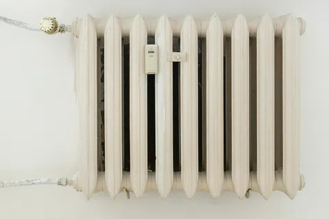 Close-up of an old white cast iron radiator mounted on a wall with visible control valve and pipes.