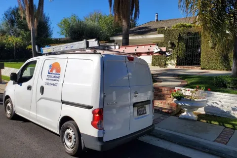 White service van with ladders on top parked on a sunny suburban street near a landscaped home.