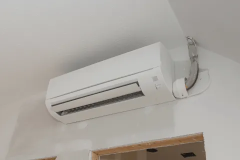 White wall-mounted air conditioner unit installed above a doorway in a partially painted room.