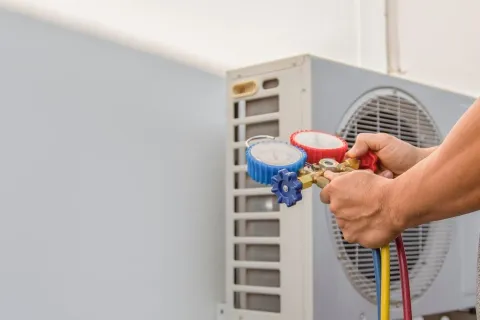 Technician adjusting gauges on an outdoor air conditioning unit for HVAC maintenance and repair.