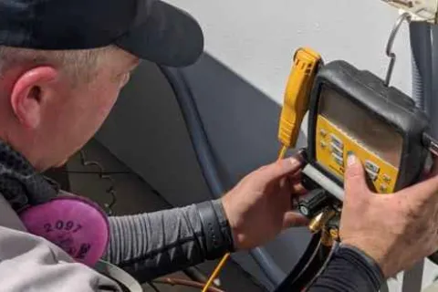 Technician adjusting HVAC system with a digital manifold gauge for maintenance and pressure measurement.