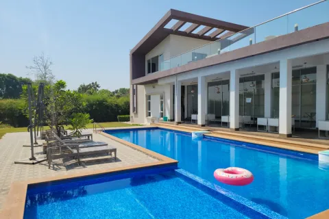 Modern house with a large blue swimming pool, poolside loungers, and a pink donut float under clear sky.