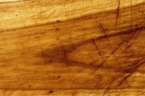 Close-up of a wooden surface with multiple scratches and worn texture in warm brown tones.