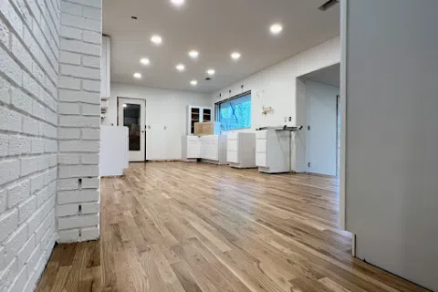 Spacious modern kitchen under construction with light wood flooring, white cabinets, and recessed ceiling lights.