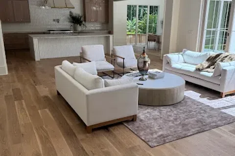 Modern living room with white sofas, armchairs, round coffee table, wooden floor, and open kitchen in background