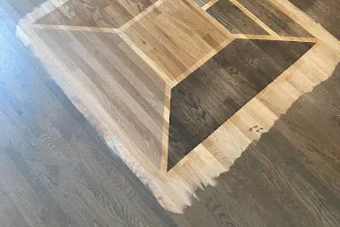 Wooden floor with a 3D illusion square design creating depth and shadow effects in a room corner.