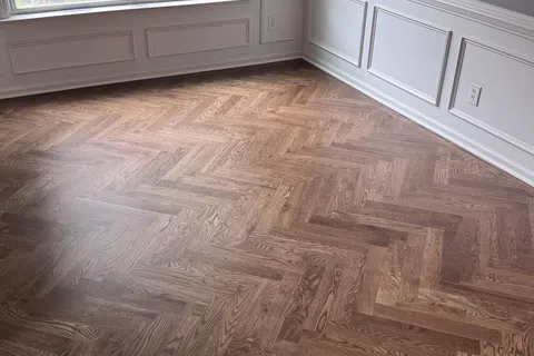 Bright room with large windows, white wainscoting, and polished herringbone wood flooring.