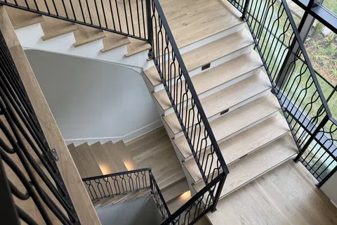 Modern wooden staircase with black metal railings inside a bright room with large windows