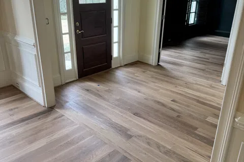 Entrance hallway with dark wooden front door, large windows, and light hardwood flooring in a bright home.