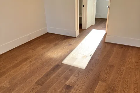 Sunlight streaming through doorway onto hardwood floor in empty room with white walls and open closets