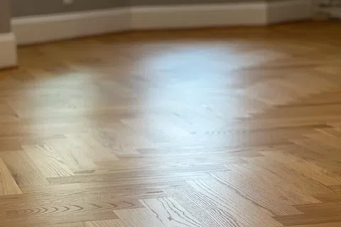 Close-up of smooth, polished hardwood floor with herringbone pattern in a bright room.