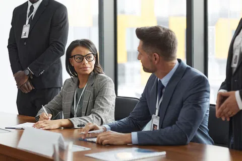 Professional businesspeople discussing and taking notes during a meeting in a modern office conference room.