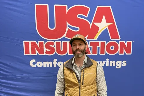 A man stands in front of a USA Insulation backdrop, promoting comfort and savings.