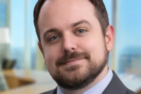 Smiling professional man in suit and tie near window in modern office setting with blurred background.